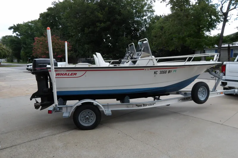 The Image of 1991 Boston Whaler SL16 boat on trailer, parked outdoors, featuring Johnson outboard motor. - 1