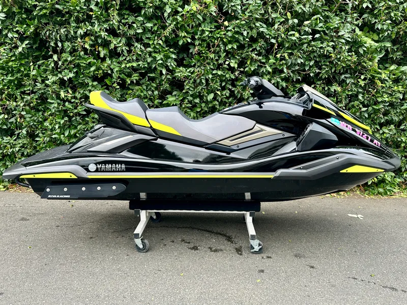 The Image of A black 2023 Yamaha FX Cruiser SVHO jet ski on a dolly, set against a green hedge. - 1