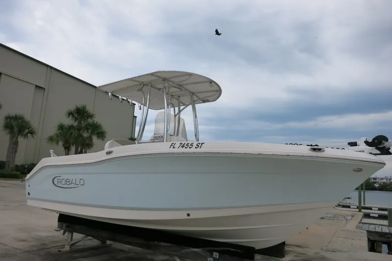 Slide: The Image of 2019 Robalo R200 Center Console boat on display, with palm trees and cloudy sky background. - 1