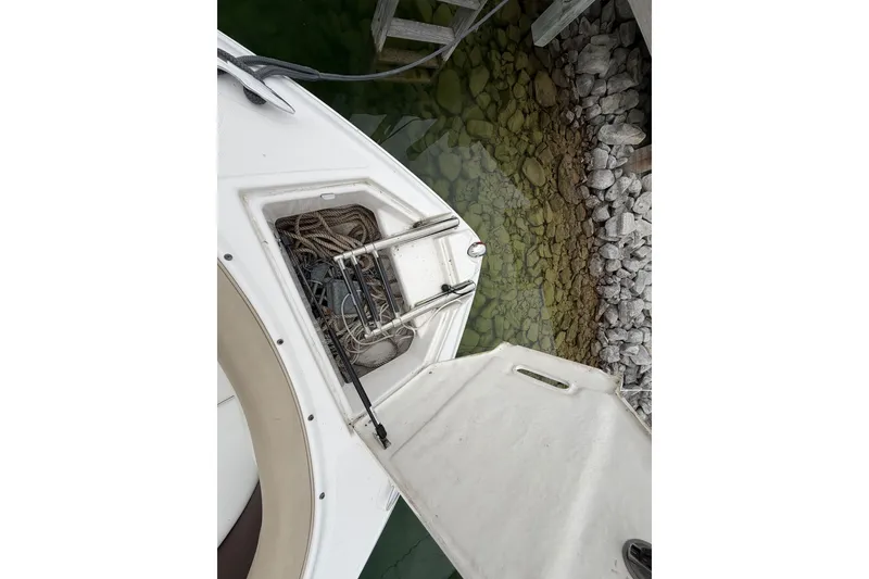 Slide: The Image of 2016 Regal 2700 ES Bowrider boat with open storage compartment, docked by rocky shoreline. - 28