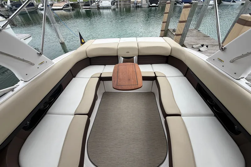 Slide: The Image of 2016 Regal 2700 ES Bowrider interior with cushioned seating and wooden table at dock. - 30