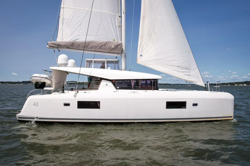 The Image of A white 2017 Lagoon 42 sailing yacht glides on calm waters under a clear blue sky. - 0