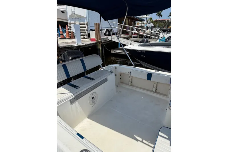 Slide: The Image of 2002 Sea Fox 230 Walk Around boat interior at marina, featuring seating and docked vessels. - 11