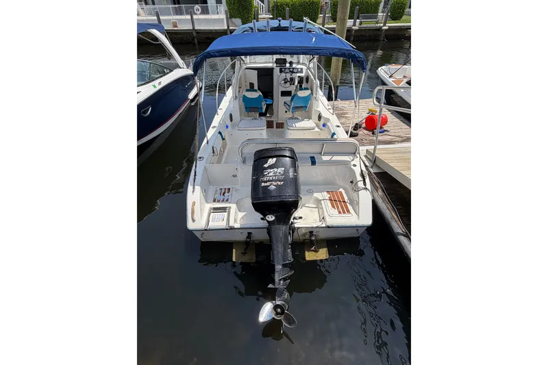 Slide: The Image of 2002 Sea Fox 230 Walk Around boat docked, featuring blue canopy and outboard motor. - 5