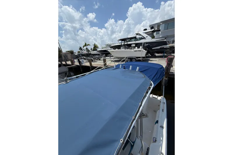 Slide: The Image of 2002 Sea Fox 230 Walk Around boat docked with blue cover under a cloudy sky. - 32