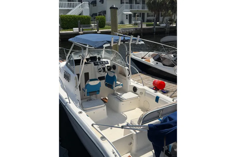 Slide: The Image of 2002 Sea Fox 230 Walk Around boat docked, featuring blue seating and canopy. - 6