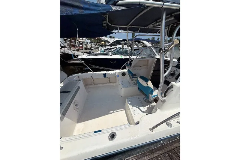 Slide: The Image of 2002 Sea Fox 230 Walk Around boat interior, featuring seating and helm, docked at marina. - 9