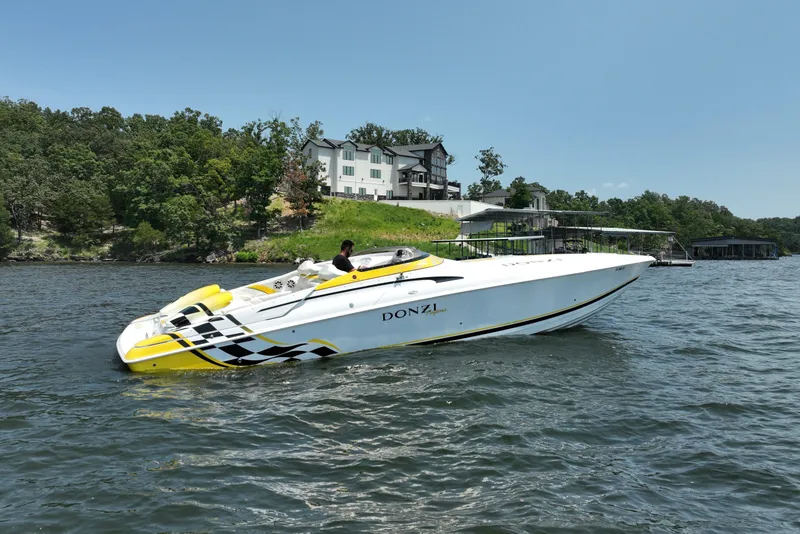 Slide: The Image of 2002 Donzi 38 Daytona speedboat on a lake, with houses and trees in the background. - 2