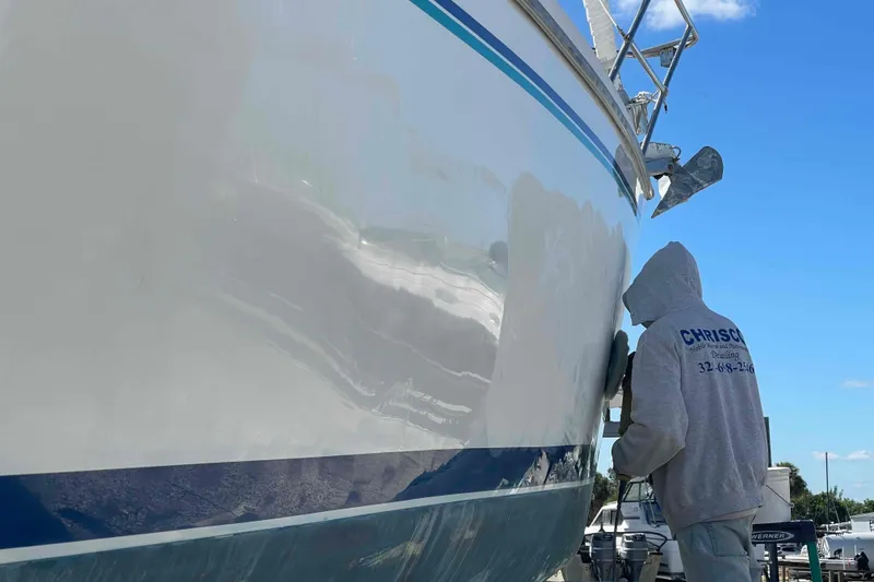 Slide: The Image of Person polishing a Catalina 320 sailboat hull under a clear blue sky. - 44