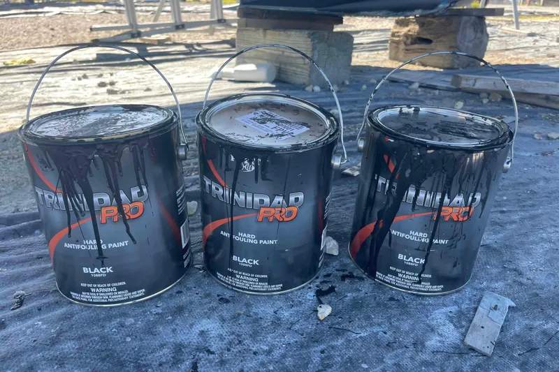 Slide: The Image of Three cans of top-f-the-line Trinidad Pro black antifouling paint on a tarp. - 42