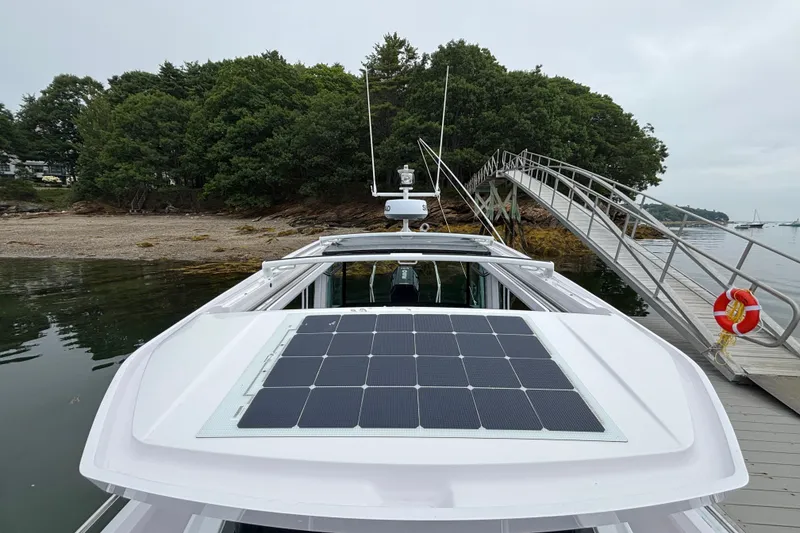 Slide: The Image of 2025 Axopar 29 XC Cross Cabin with solar panel docked near a wooded shoreline. - 19
