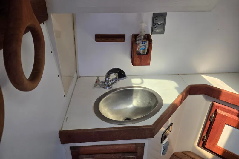 Slide: The Image of Compact sink area in a 1989 Catalina 34 sailboat, featuring wooden accents and a mounted soap dispenser. - 25