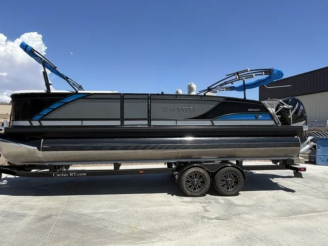 Slide: The Image of A 2022 Godfrey Pontoons Monaco 255 DFL 27 In. on a trailer. It features a sleek design with blue accents. - 18