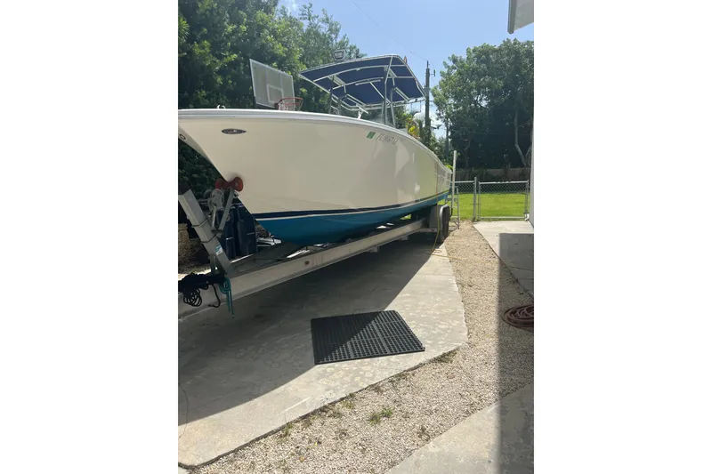 Slide: The Image of 2000 Ocean Runner 27 boat on trailer, parked in driveway, surrounded by greenery. - 15