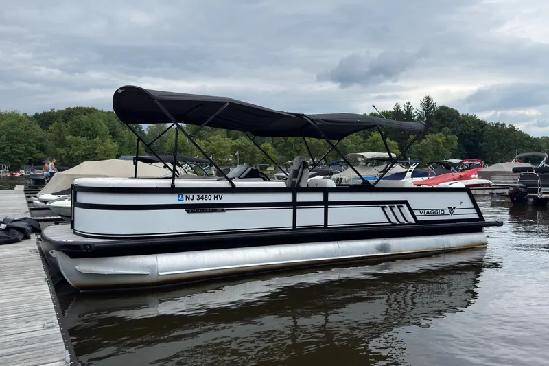 The Image of 2026 Viaggio Diamante S 26 pontoon boat docked on a lake under cloudy skies. - 0