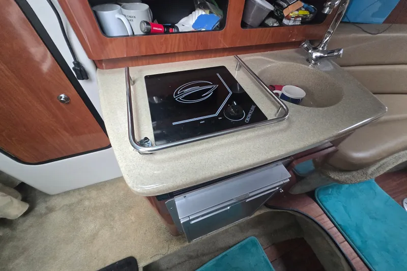 Slide: The Image of 2014 Crownline 264 CR boat interior with kitchenette, featuring a stove and sink. - 23