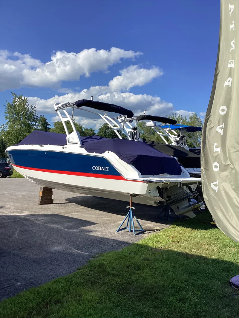 Slide: The Image of A 2027 Cobalt R26 boat on a parking lot, supported by stands, with blue covers. - 8