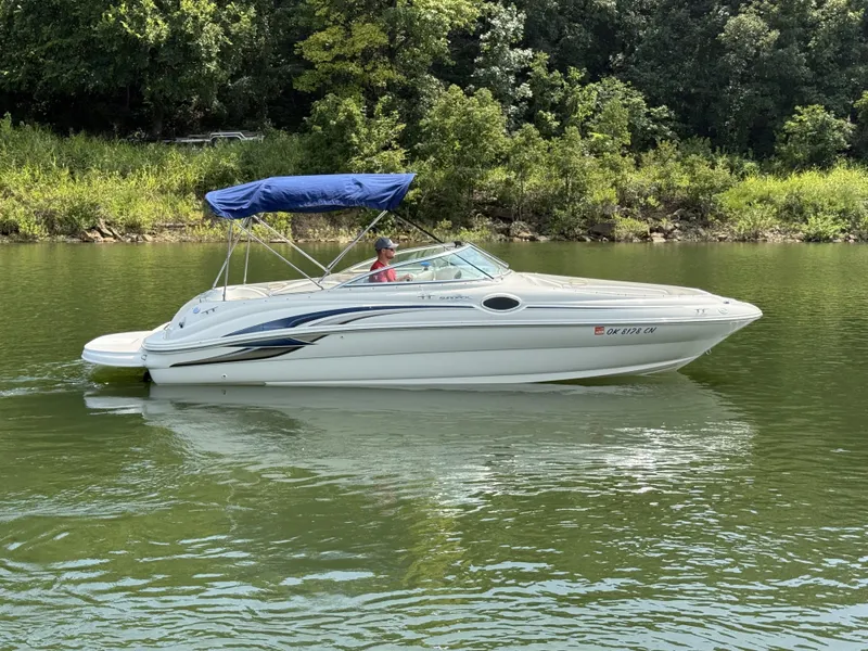 Slide: The Image of A white 2000 Sea Ray 240 Sundeck boat with a blue sunshade cruising on a calm river. - 2