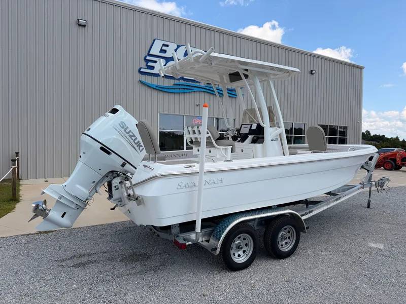 Slide: The Image of A white Savannah 210X boat on a trailer with a Suzuki engine, parked outside a building. - 1