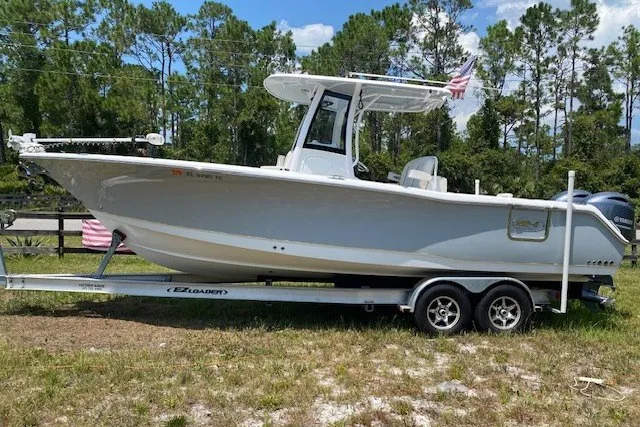 The Image of 2022 Sea Hunt Gamefish 27CB boat on trailer, parked outdoors with trees in background. - 1