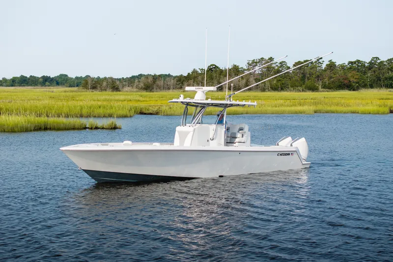 The Image of 2025 Contender 32 ST boat cruising on a serene lake with lush greenery. - 0