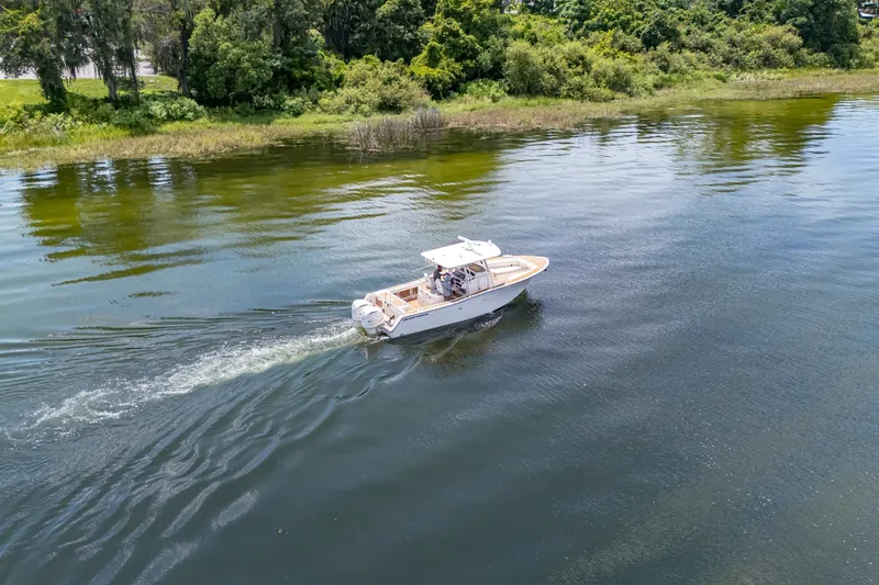 Slide: The Image of 2015 Grady-White Canyon 306 boat cruising on a serene lake with lush greenery. - 18