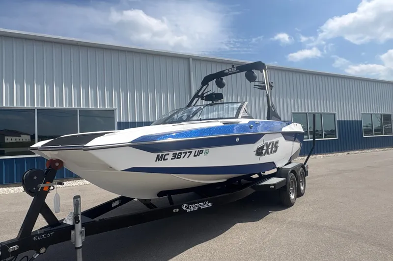Slide: The Image of 2021 Axis A20 boat on trailer outside a metal building under a blue sky. - 2