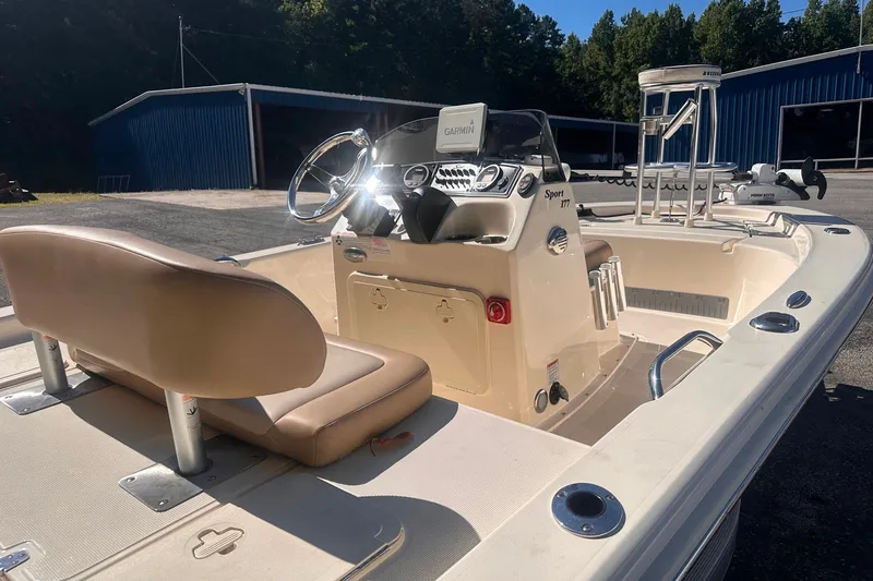 Slide: The Image of 2022 Ocean Scout Sport 177 boat interior with steering wheel and seating, parked near blue building. - 16