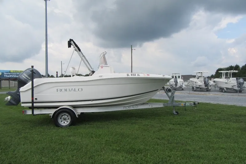 Slide: The Image of 2018 Robalo R180 Center Console boat on trailer, parked on grass under cloudy sky. - 2