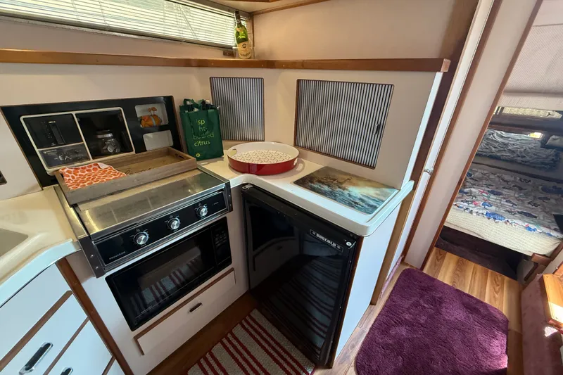 Slide: The Image of 1989 Sea Ray 340 Sundancer galley with stove, fridge, and cozy cabin interior. - 28
