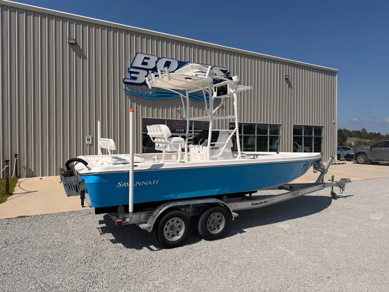 The Image of A blue and white Savannah 220 IS boat on a trailer in front of a building with a large sign. - 0