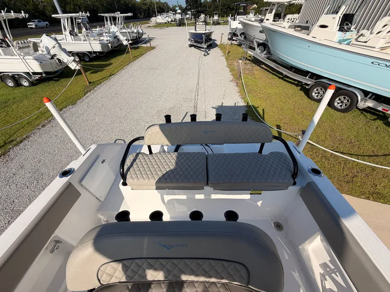Slide: The Image of The image shows the cockpit of a 2027 Savannah 2200 Offshore boat. It features cushioned seating and is parked on a gravel path. - 13