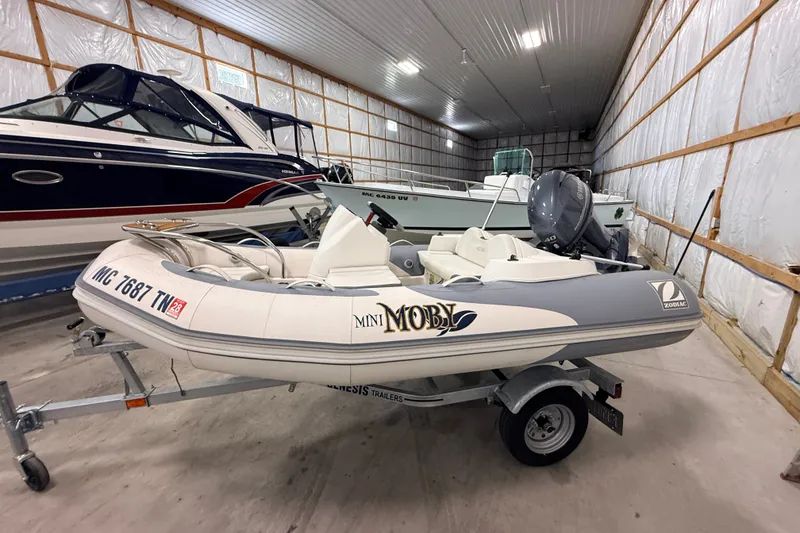 The Image of 2013 Zodiac Yachtline 2 Deluxe 340 inflatable boat in storage, featuring a trailer and outboard motor. - 0