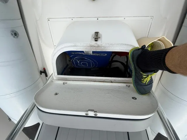 Slide: The Image of An open storage compartment on a 2022 Ribcraft 6.5 boat with a foot in sneakers. - 8