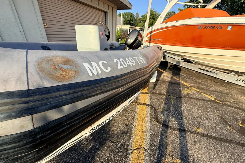 Slide: The Image of 2014 Zodiac Milpro SR 4.70 inflatable boat parked beside an orange boat on a trailer. - 23
