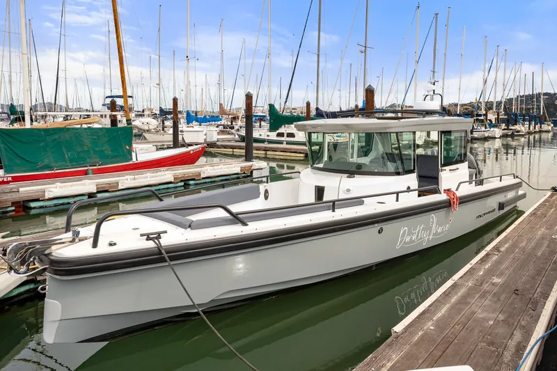 The Image of 2021 Axopar 28 Cabin boat docked in a marina with sailboats in the background. - 0
