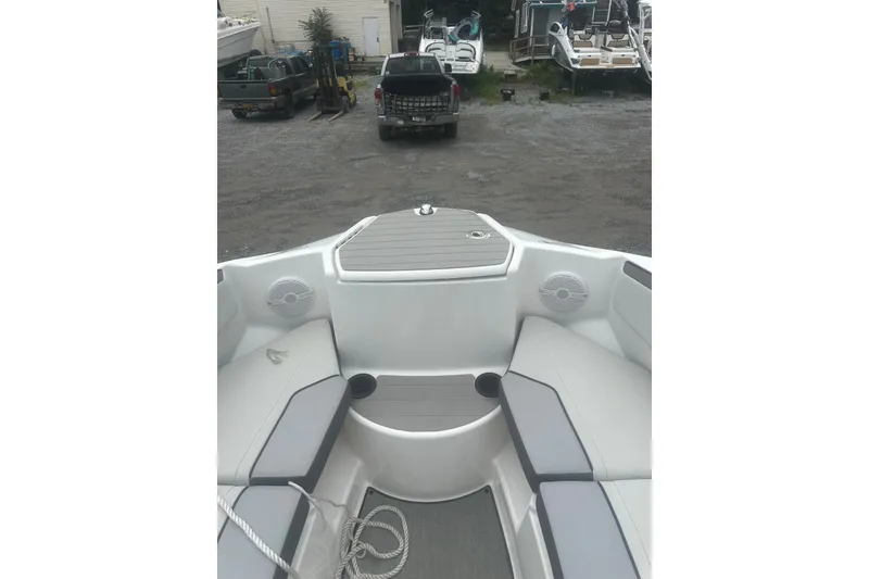 Slide: The Image of 2025 Yamaha Boats AR220 interior with seating and storage, parked near other boats and vehicles. - 9
