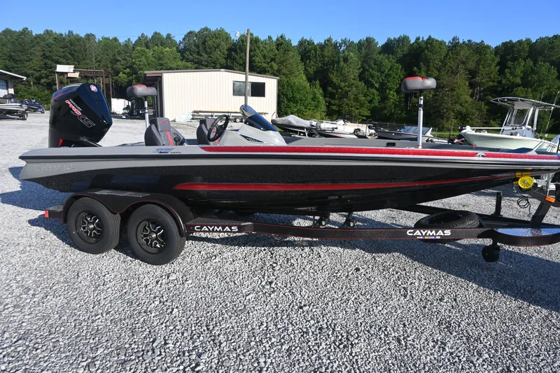 The Image of A 2027 Caymas 201 Pro boat on a trailer in a gravel lot, surrounded by trees. - 1