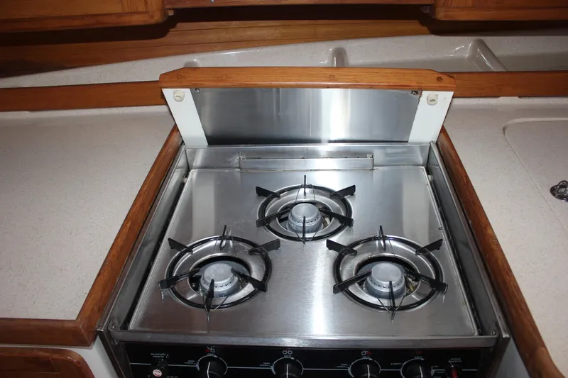 Slide: The Image of A stainless steel stove with three burners in a boat galley, surrounded by wooden cabinets. - 28