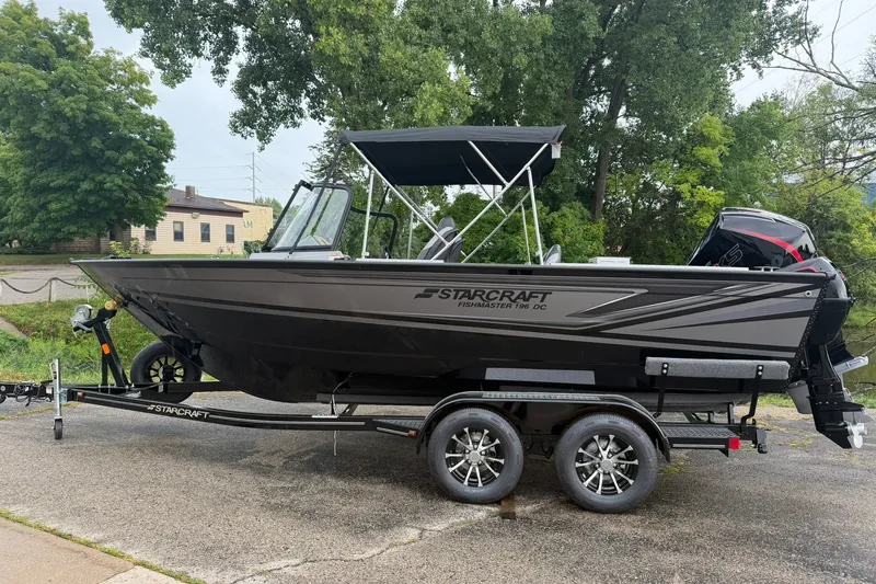 The Image of 2027 Starcraft Fishmaster 196 boat on trailer, parked outdoors with trees in background. - 1