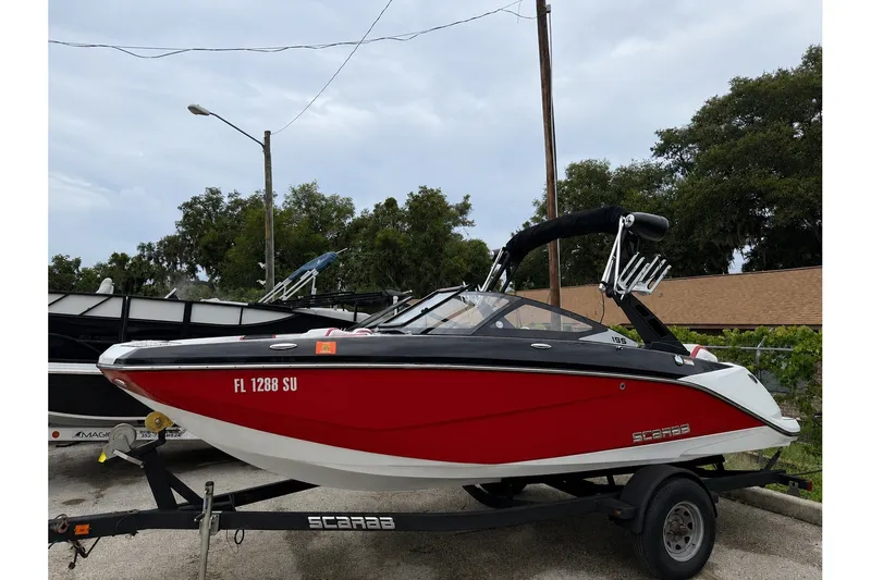 The Image of 2020 Scarab 195 Wake ID boat in red on a trailer, parked outdoors. - 0