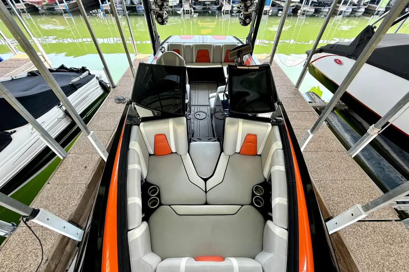 Slide: The Image of 2018 Malibu Wakesetter 21 MLX boat interior with orange and gray seating at a dock. - 24