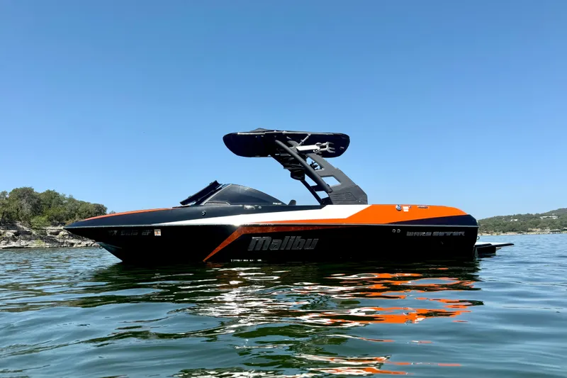 Slide: The Image of 2018 Malibu Wakesetter 21 MLX boat on calm water under clear blue sky. - 3