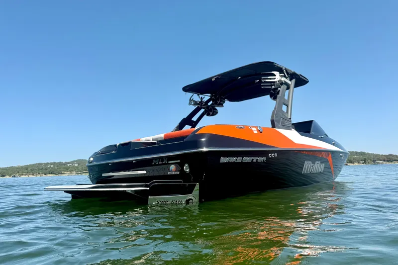 Slide: The Image of 2018 Malibu Wakesetter 21 MLX boat on calm water under clear blue sky. - 6