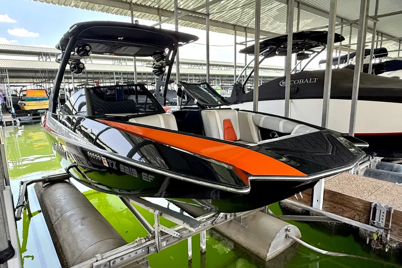 Slide: The Image of 2018 Malibu Wakesetter 21 MLX boat in dock, featuring sleek black and orange design. - 18