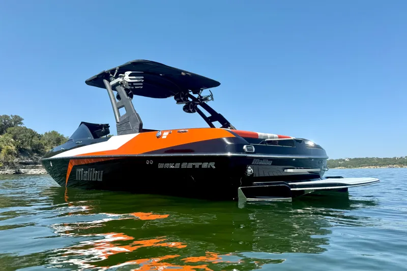 Slide: The Image of 2018 Malibu Wakesetter 21 MLX boat on calm water under clear blue sky. - 4