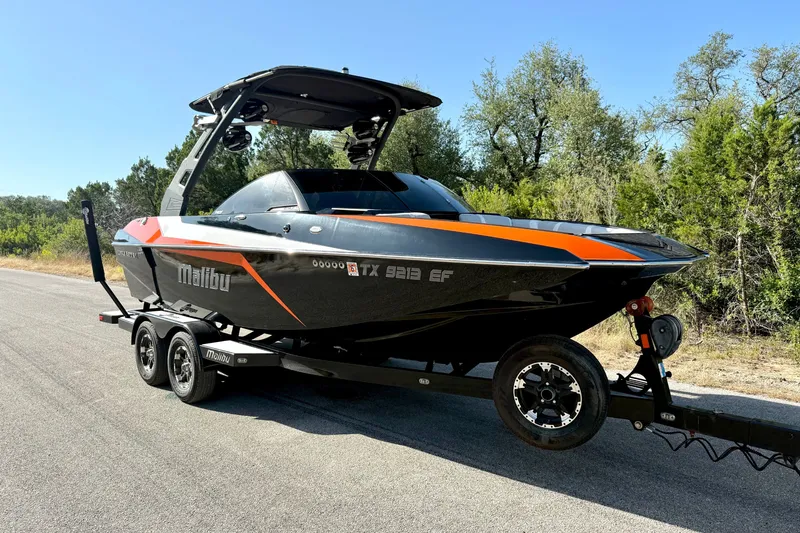 Slide: The Image of 2018 Malibu Wakesetter 21 MLX boat on trailer, parked on a sunny road. - 14