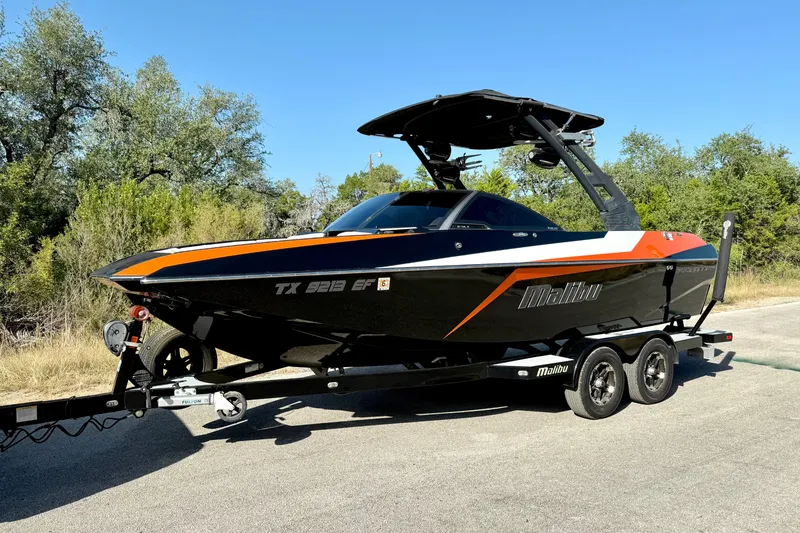 Slide: The Image of 2018 Malibu Wakesetter 21 MLX boat on trailer, black and orange design, parked outdoors. - 9