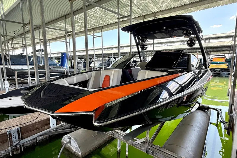 Slide: The Image of 2018 Malibu Wakesetter 21 MLX boat with orange and black design in a marina. - 19