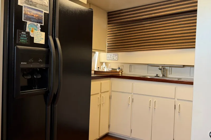 Slide: The Image of Kitchen area of 1986 Hatteras 63 Cockpit Motor Yacht with black fridge and white cabinets. - 26